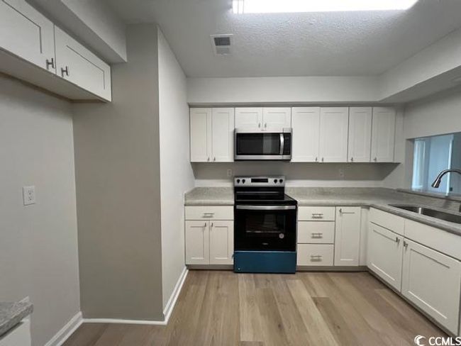 Kitchen featuring a sink, appliances with stainless steel finishes, light wood-style floors, and white cabinetry | Image 25