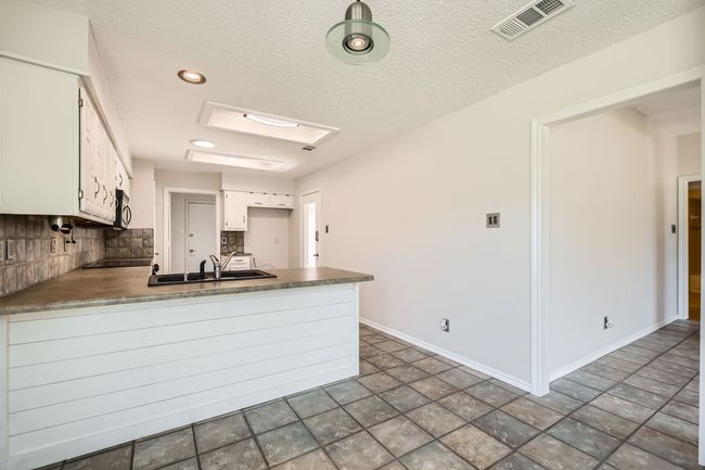 Kitchen with a peninsula, backsplash, white cabinets, a textured ceiling, and stainless steel microwave | Image 9