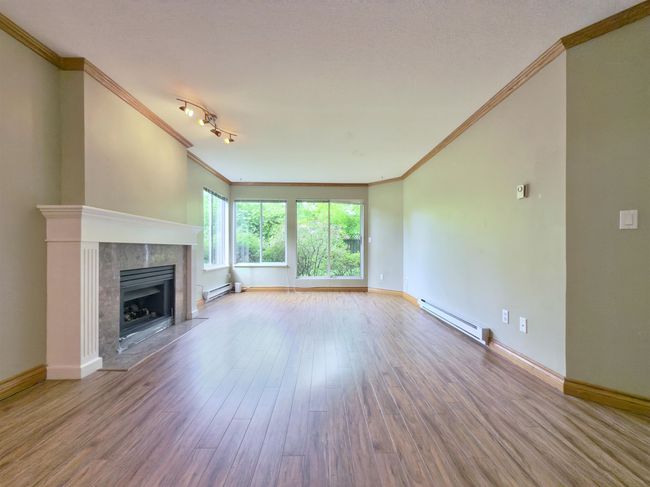 Unfurnished living room with baseboard heating, crown molding, a tile fireplace, wood finished floors, and baseboards | Image 5