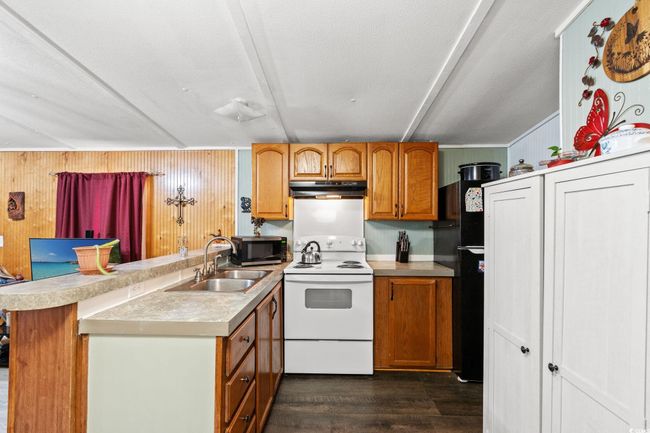 Kitchen featuring electric range, a sink, stainless steel microwave, under cabinet range hood, and a peninsula | Image 11
