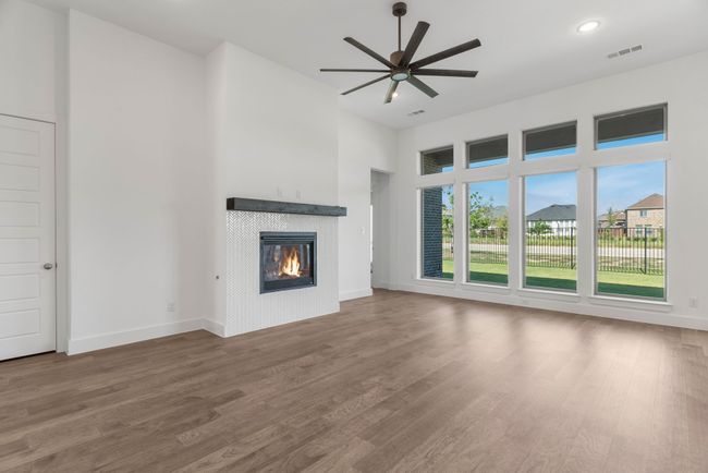 Unfurnished living room featuring a tiled fireplace, wood finished floors, a high ceiling, ceiling fan, and baseboards | Image 22