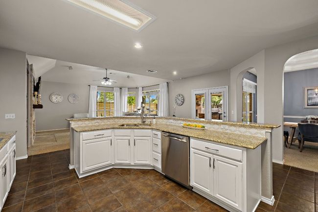 Kitchen with stainless steel dishwasher, arched walkways, a sink, a ceiling fan, and white cabinetry | Image 13
