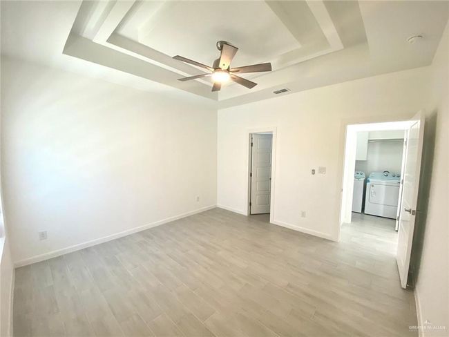 Unfurnished bedroom featuring a tray ceiling, washer and clothes dryer, light wood-type flooring, and a ceiling fan | Image 12