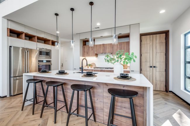 Kitchen with appliances with stainless steel finishes, modern cabinets, light countertops, a kitchen breakfast bar, and hanging light fixtures | Image 10