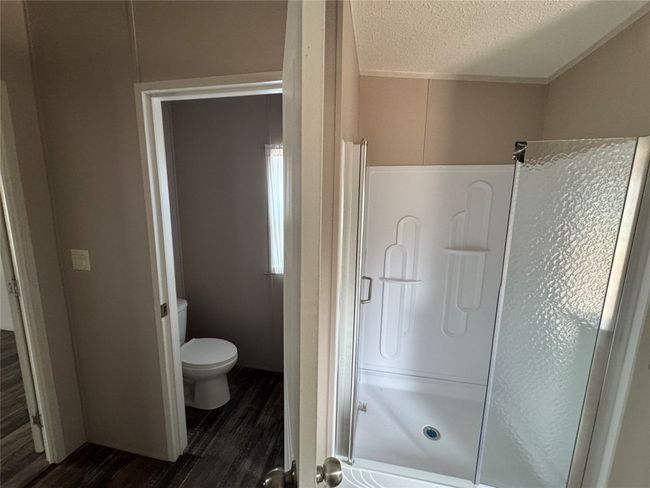 Bathroom with wood finished floors, a textured ceiling, a shower stall, and toilet | Image 8