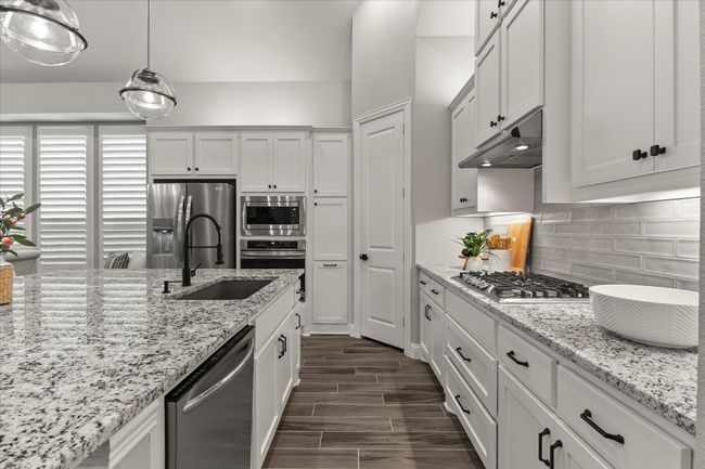 Kitchen featuring stainless steel appliances, under cabinet range hood, tasteful backsplash, dark wood-type flooring, white cabinetry, gas cooktop, granite counters | Image 16