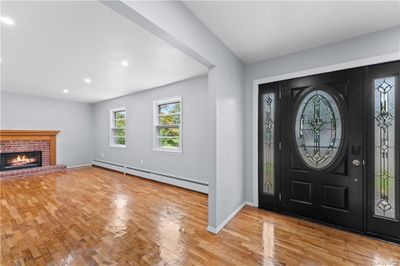 Foyer entrance featuring a baseboard radiator, a brick fireplace, and light hardwood / wood-style floors | Image 2