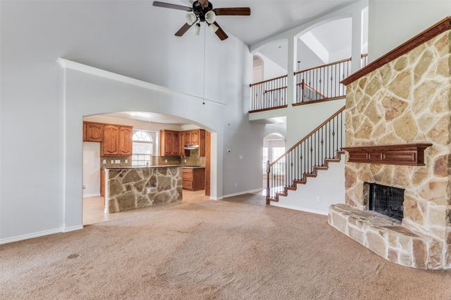 Unfurnished living room featuring light colored carpet, arched walkways, a ceiling fan, a fireplace, and a towering ceiling | Image 7