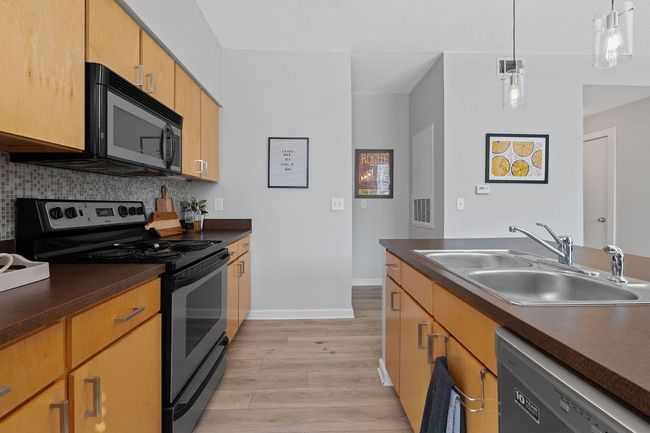 Kitchen featuring stainless steel electric stove, dishwashing machine, black microwave, light wood-style floors, and dark countertops | Image 11