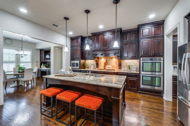 Hand-scraped wood floors continue into the kitchen, where functional upgrades like an island sink, double ovens, and a 6-burner gas stove elevate both style and efficiency. | Image 11