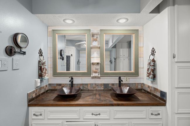 This primary bathroom features a double vanity with stylish vessel sinks and dark wood countertops. Framed mirrors and elegant lighting add a touch of sophistication, while the light cabinetry offers ample storage. | Image 26