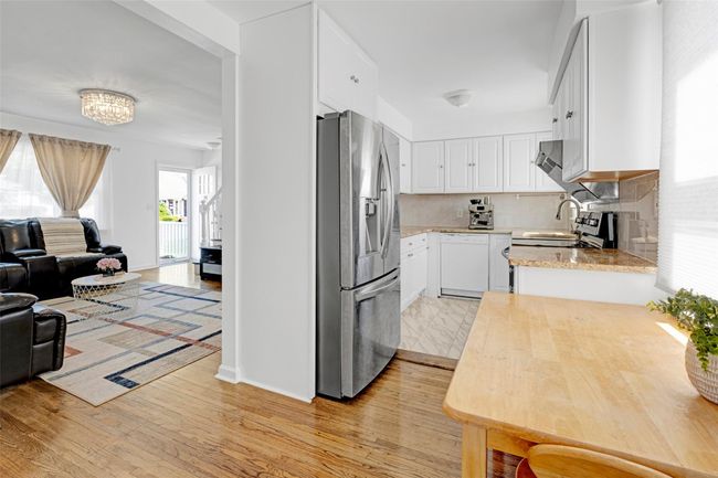 Kitchen featuring stainless steel refrigerator with ice dispenser, white dishwasher, open floor plan, light wood-type flooring, and white cabinets | Image 8