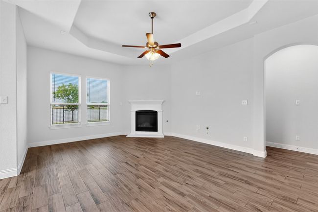 Unfurnished living room with a raised ceiling, arched walkways, wood finished floors, and a ceiling fan | Image 14