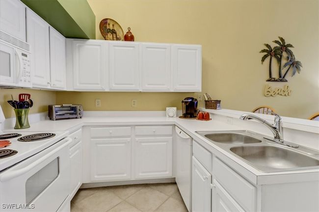 Kitchen featuring white appliances, light tile patterned flooring, a peninsula, and white cabinetry | Image 10
