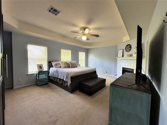Master Bedroom featuring a raised ceiling, light colored carpet, a tile fireplace, baseboards, and a textured ceiling | Image 28