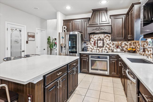 Kitchen with stainless steel appliances, a sink, light countertops, premium range hood, and decorative backsplash | Image 7