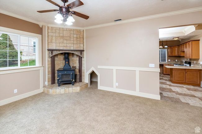 Unfurnished living room with ceiling fan, light carpet, ornamental molding, and a wood stove | Image 34