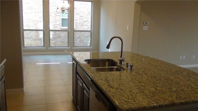 Kitchen with a sink, a kitchen island with sink, light tile patterned floors, and healthy amount of natural light | Image 7
