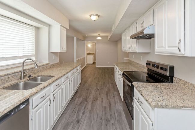 Kitchen featuring stainless steel range with electric stovetop, under cabinet range hood, white cabinets, dark wood finished floors, and light stone countertops | Image 6
