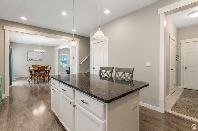Kitchen with dark wood-type flooring, white cabinetry, hanging light fixtures, and a center island | Image 8