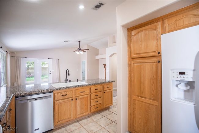 Kitchen featuring stainless steel dishwasher, a sink, white refrigerator with ice dispenser, visible vents, and vaulted ceiling | Image 9