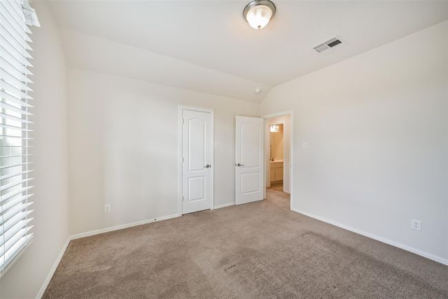 Bright, carpeted upstairs bedroom 2 with neutral walls, featuring two doors—one leading to a bathroom. A window with blinds allows natural light in, and a ceiling light fixture adds illumination. | Image 25