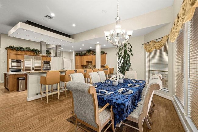This photo showcases a spacious, open-concept dining and kitchen area with modern appliances, ample cabinetry, and elegant lighting. The breakfast space features a large table set for entertaining, complemented by a sophisticated chandelier. The room is well-lit and inviting, with a warm color palette and hardwood flooring. | Image 11