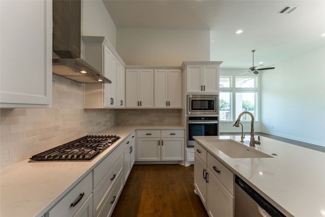 Kitchen with appliances with stainless steel finishes, wall chimney exhaust hood, a ceiling fan, white cabinets, and dark wood-style flooring | Image 17