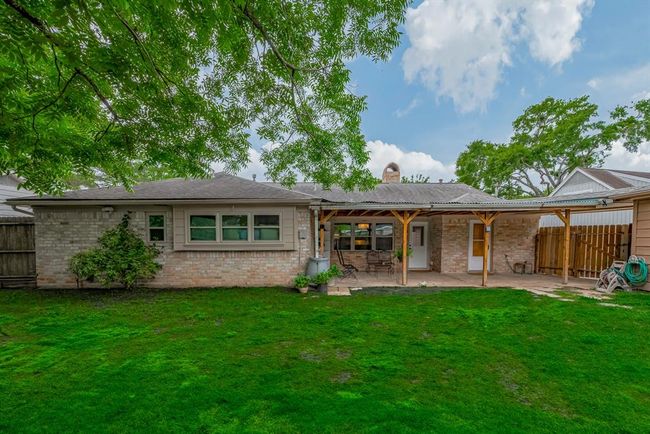 Spacious backyard with lush green grass and a large tree, featuring a covered patio ideal for outdoor relaxation and entertainment. | Image 40