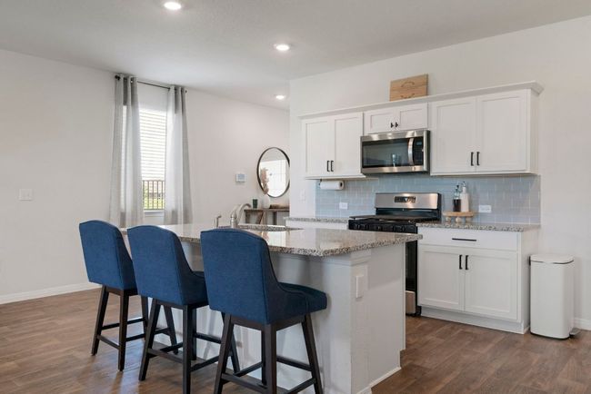 Kitchen featuring stainless steel appliances, tasteful backsplash, dark wood-style flooring, an island with sink, and white cabinetry | Image 13