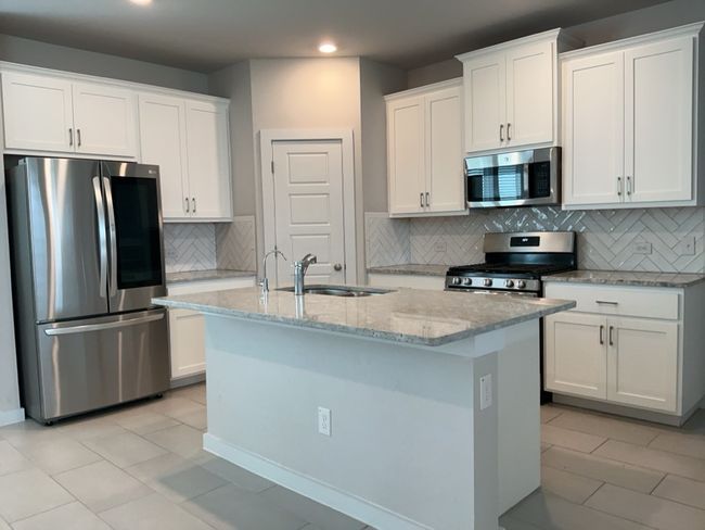 Kitchen featuring stainless steel appliances, recessed lighting, light stone countertops, a center island with sink, and white cabinets | Image 5