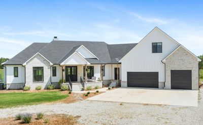 Modern farmhouse with a porch, a front lawn, and a garage | Image 1