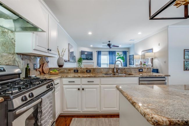 Kitchen featuring appliances with stainless steel finishes, exhaust hood, ornamental molding, light stone countertops, and white cabinetry | Image 13