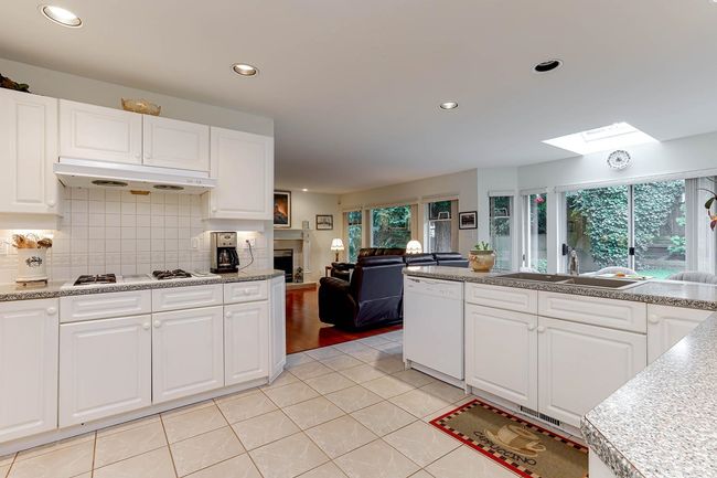 Kitchen featuring white appliances, a skylight, under cabinet range hood, a fireplace, and a sink | Image 11
