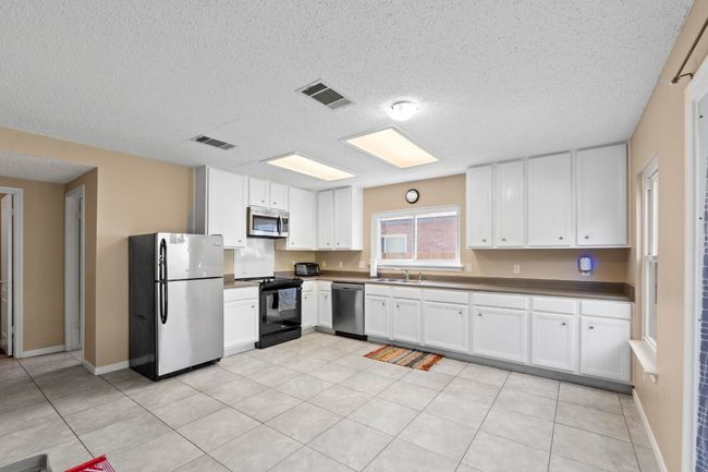 Kitchen with stainless steel appliances, a sink, a textured ceiling, white cabinetry, and dark countertops | Image 11