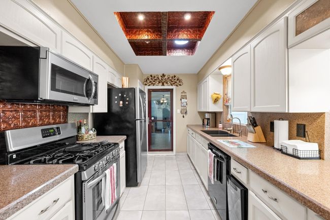 Kitchen with light tile patterned floors, white cabinets, a sink, stainless steel appliances, and backsplash | Image 11