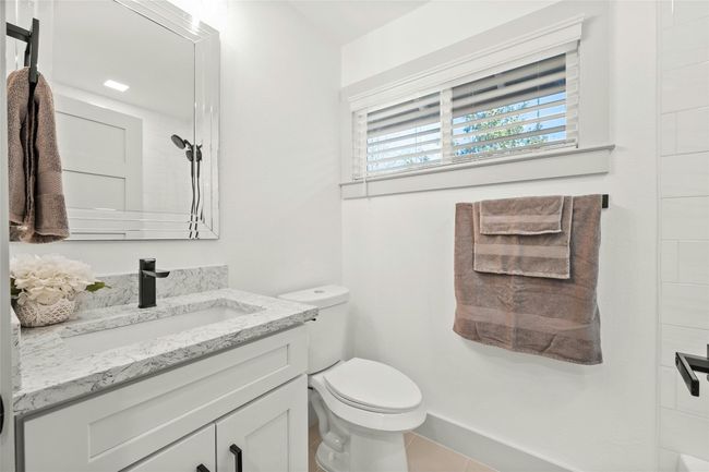 The spacious additional bathroom is located between the additional bedrooms. It offers a large vanity with additional quartz countertop space, elegant tile flooring, gray cabinets with 5-inch black cabinets pulls, and a tub/shower combo with a tile surround. | Image 24