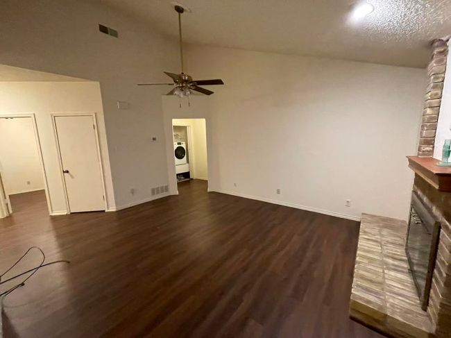 Unfurnished living room featuring washer / clothes dryer, dark wood-style floors, ceiling fan, and a fireplace | Image 4