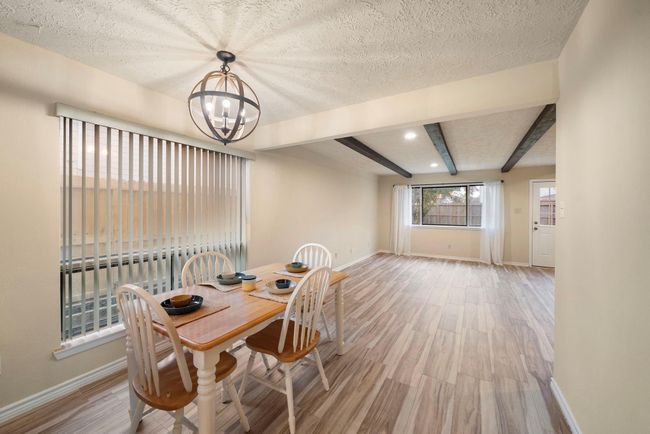 Large windows and vertical blinds flood the spacious dining area with natural light, while wood-style tile flooring and exposed ceiling beams flow seamlessly into the adjacent living space. | Image 14