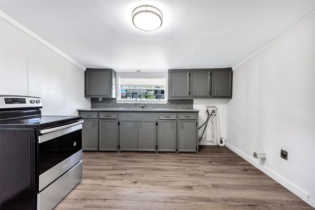 Kitchen with stainless steel electric stove, gray cabinetry, light wood-style floors, ornamental molding, and backsplash | Image 21