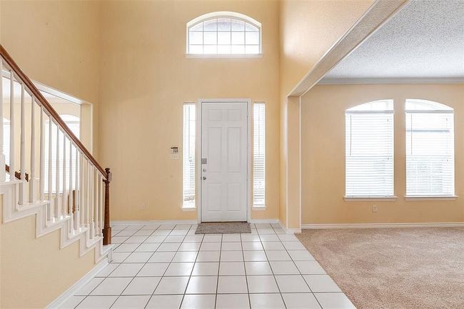 Entrance foyer with light tile patterned flooring, baseboards, a high ceiling, and stairs | Image 11