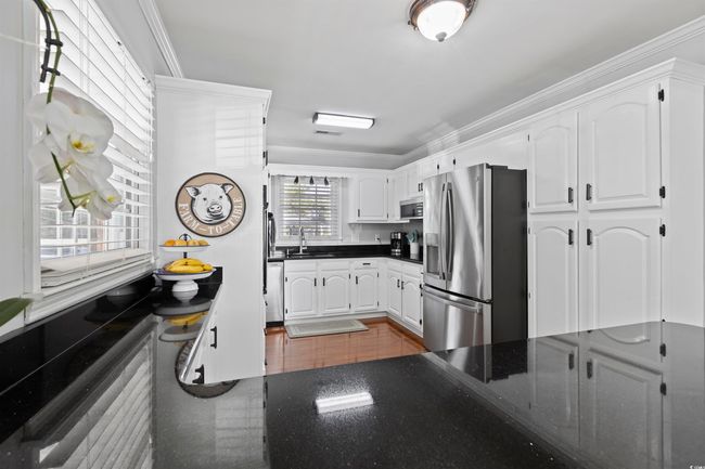 Kitchen with appliances with stainless steel finishes, a sink, crown molding, white cabinets, and dark stone countertops | Image 9