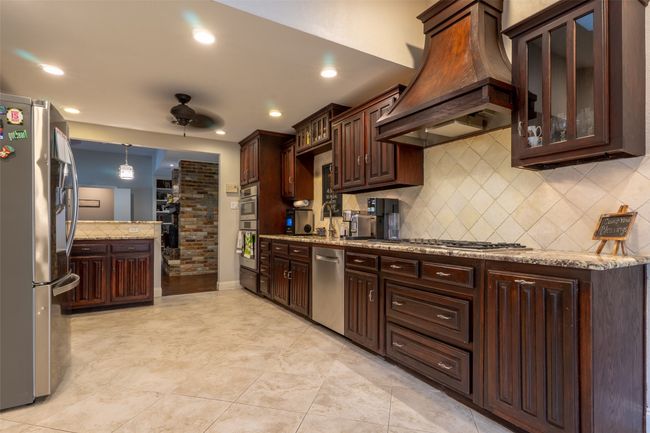 Kitchen featuring premium range hood, stainless steel appliances, ceiling fan, dark brown cabinets, and backsplash | Image 10