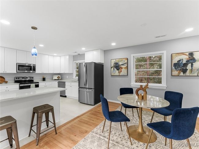 Kitchen featuring appliances with stainless steel finishes, white cabinetry, hanging light fixtures, and visible vents | Image 16