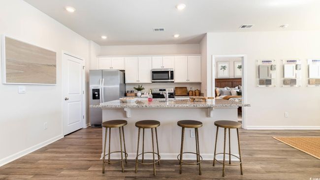 Kitchen with visible vents, a center island with sink, a kitchen bar, white cabinets, and appliances with stainless steel finishes | Image 6