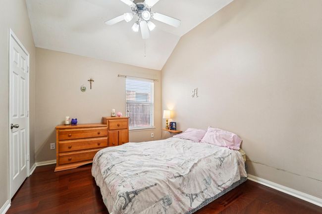 Cozy bedroom with neutral walls, hardwood floors, and a ceiling fan. Features a window for natural light, a wooden dresser, and a comfortable bed. | Image 21