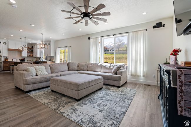 Living area featuring wood finished floors, a textured ceiling, ceiling fan with notable chandelier, baseboards, and recessed lighting | Image 12