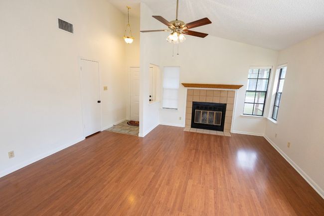 Unfurnished living room with ceiling fan, wood finished floors, a fireplace, baseboards, and high vaulted ceiling | Image 10
