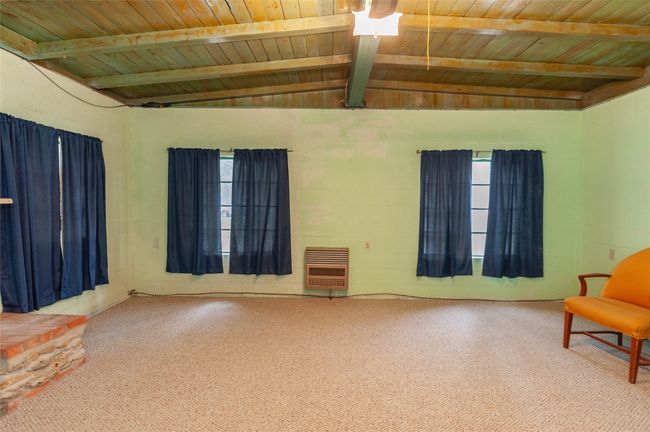 Carpeted empty room with wood ceiling, vaulted ceiling with beams, and heating unit | Image 14