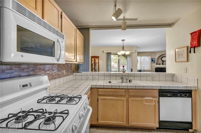 Kitchen with a sink, decorative backsplash, white appliances, a peninsula, and a notable chandelier | Image 33
